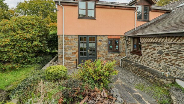 A two-story house with stone and brick exterior walls, a stone staircase leading to the entrance, and a well-maintained garden with various plants and shrubs. - Penybont Apartment (Aberystwyth)