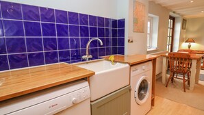 A compact kitchen with a Bosch dishwasher, a washing machine, and a sink with a yellow brush. - Penybont Apartment (Aberystwyth)