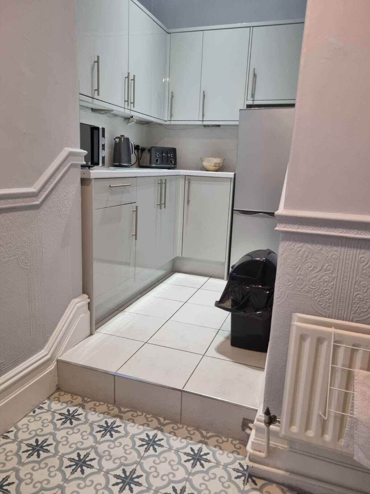 A compact kitchen with white cabinets, a microwave, a kettle, and a trash bin.