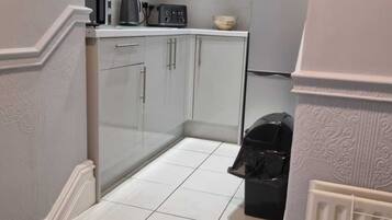 A compact kitchen with white cabinets, a microwave, a kettle, and a trash bin.