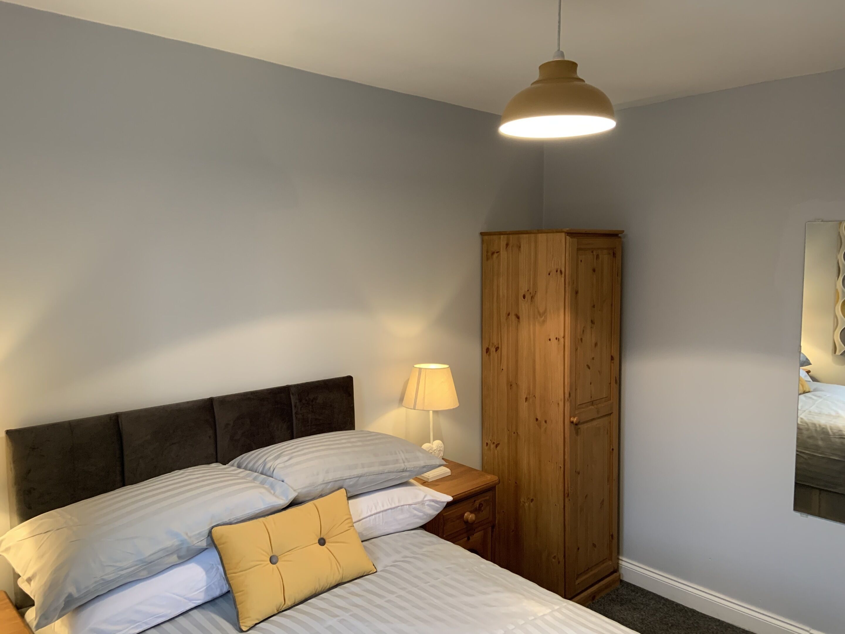 A bedroom with a bed, a wooden wardrobe, a nightstand with a lamp, and a ceiling light fixture.