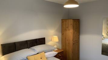 A bedroom with a bed, a wooden wardrobe, a nightstand with a lamp, and a ceiling light fixture.