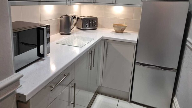 A modern kitchen with grey cabinets, a stainless steel refrigerator, a microwave, a kettle, and a toaster. - Hursley Lodge (Lincoln)