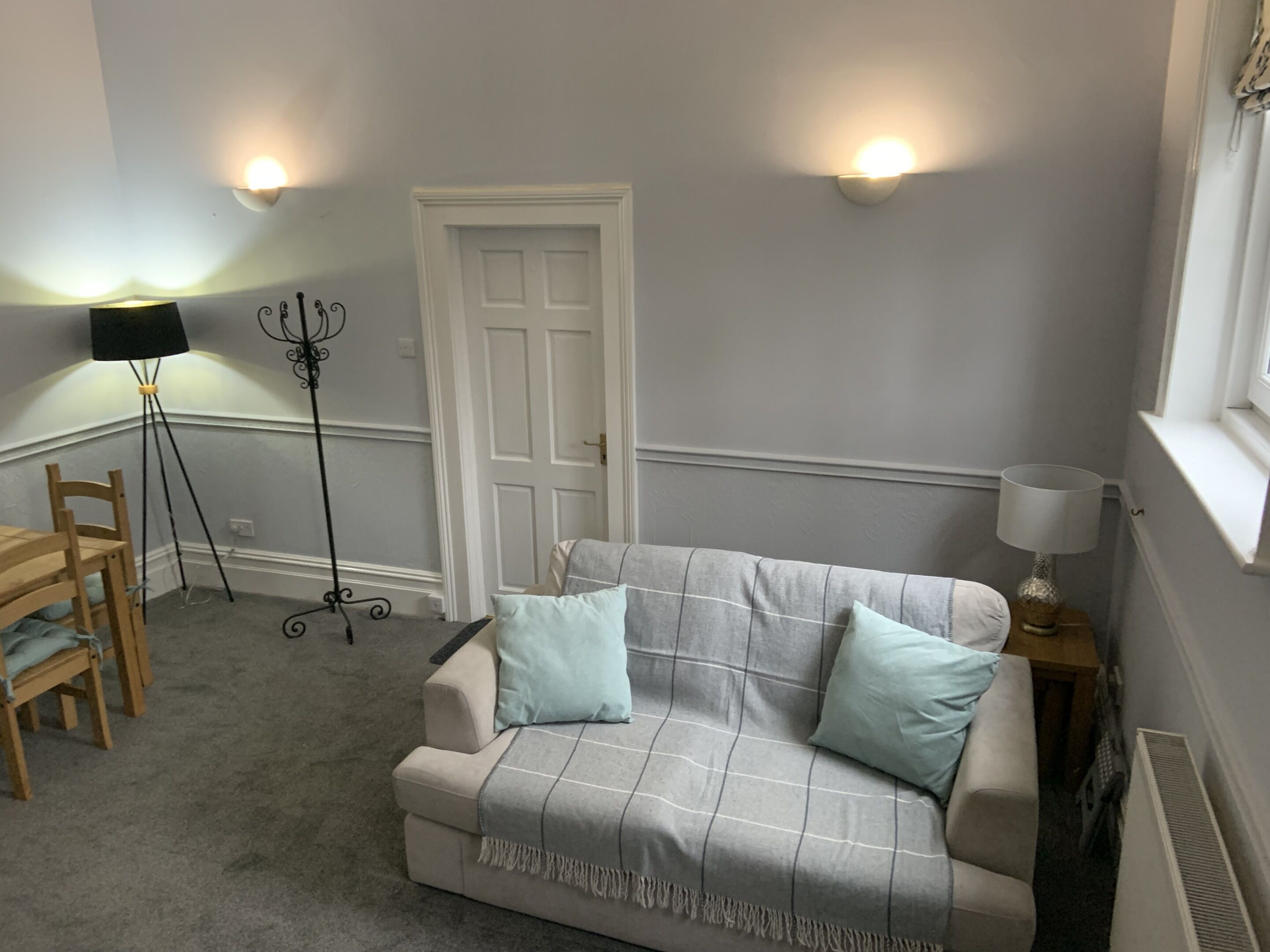 A room with a sofa, a chair, a floor lamp, a standing lamp, and a door.
