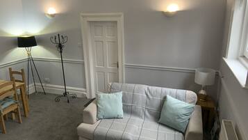A room with a sofa, a chair, a floor lamp, a standing lamp, and a door.