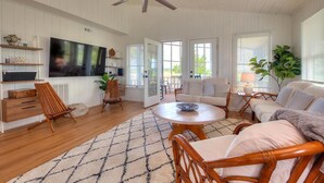 Ein geräumiges Wohnzimmer mit Deckenventilator, einem großen Flachbildfernseher, einem Holztisch und einer gemütlichen Sitzecke mit Sofa und Sesseln.