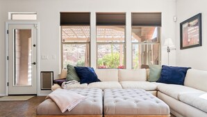 A living room with a sectional sofa, a wooden ottoman, and a door with a view of the outdoors. - Estrella Golden Oasis | Mountain view back yard! (Goodyear)