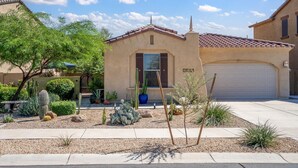 A residential house with a tiled roof, a garage, and a landscaped garden with cacti and shrubs. - Estrella Golden Oasis | Mountain view back yard! (Goodyear)