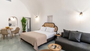 Un dormitorio moderno con cama, sofá, mesa de comedor con sillas y una planta en maceta.