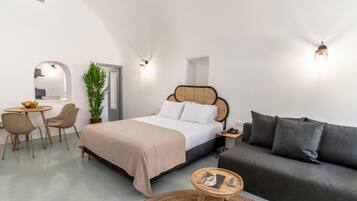 A modern bedroom with a bed, a sofa, a dining table with chairs, and a potted plant.