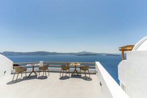 Varanda com duas cadeiras de vime e uma mesa, com vista para o mar azul e ilhas ao longe.