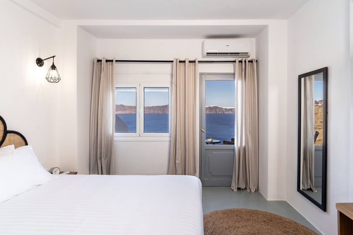 A hotel room with a bed, a window with curtains, an air conditioning unit, and a view of the sea.