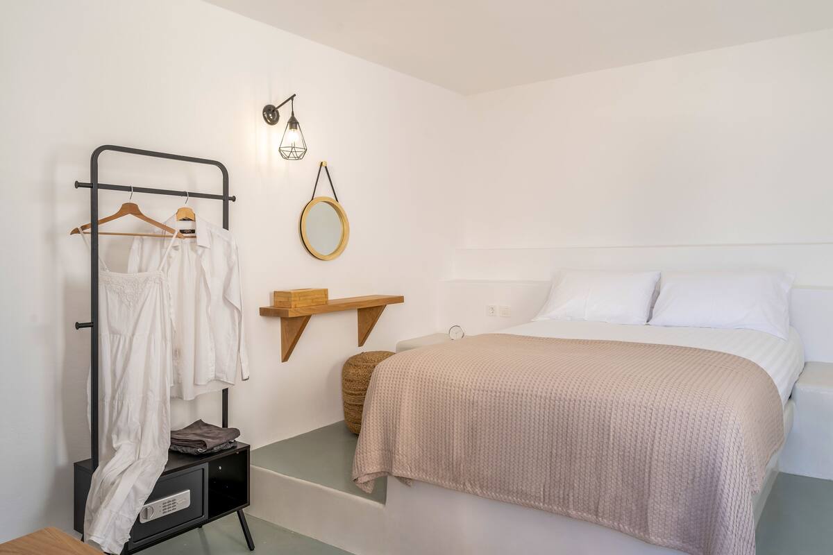 A bedroom with a bed, a hanging clothes rack, a round mirror, and a small shelf.