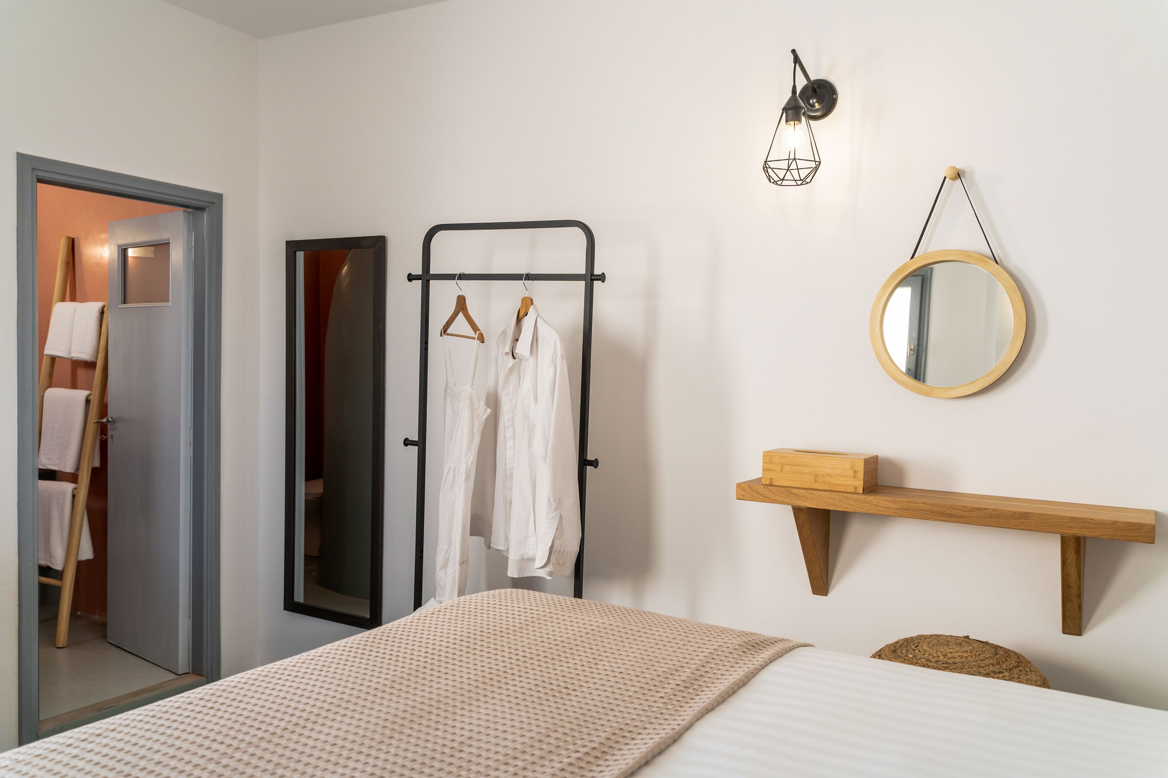 Quarto com cama, prateleira de madeira, espelho e cabideiro.