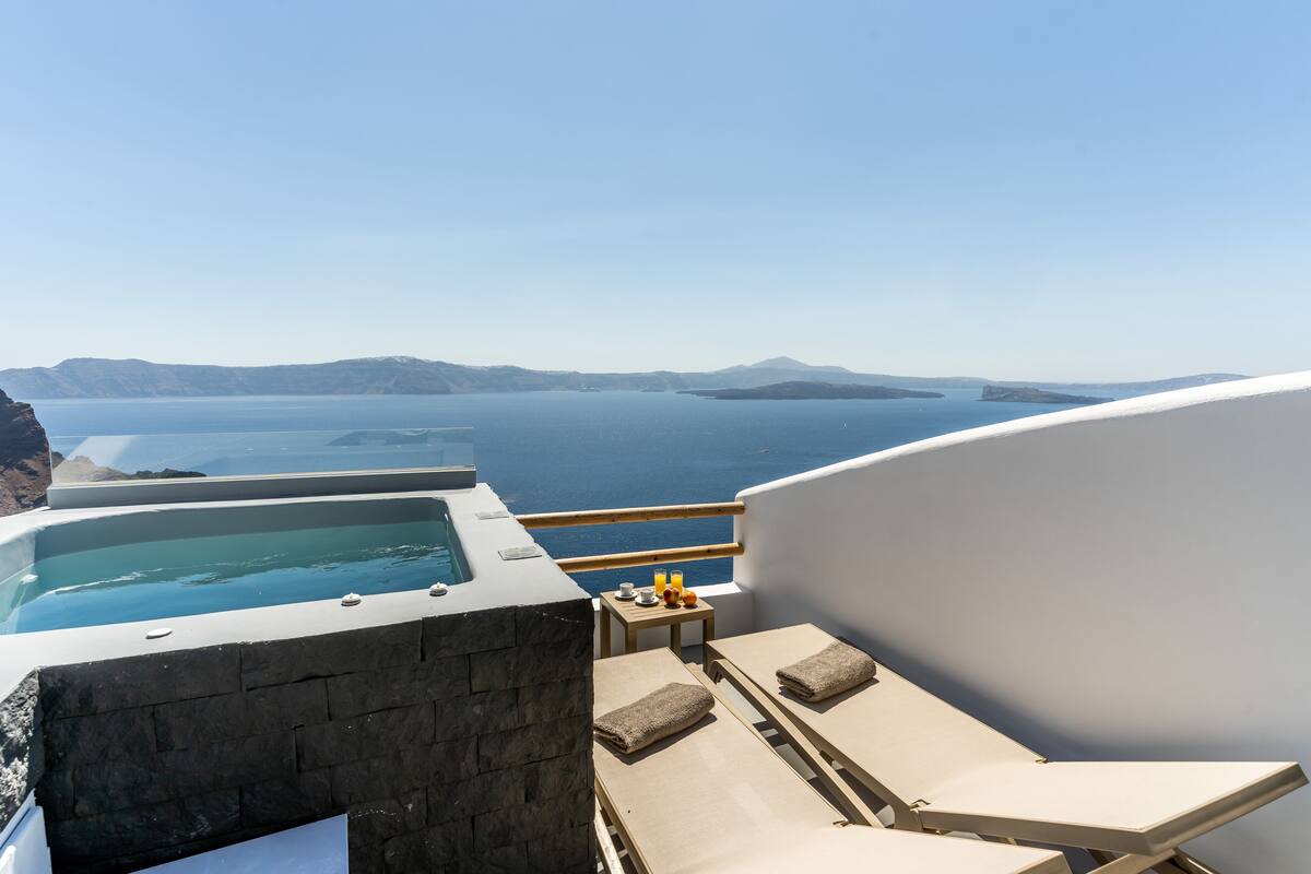 A rooftop terrace with a hot tub, lounge chairs, and a table with drinks and snacks.