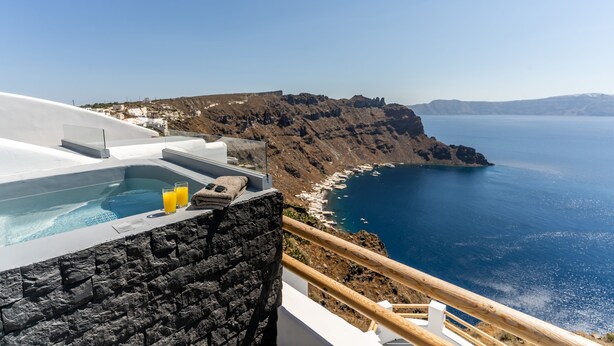 Un jacuzzi con pared de piedra, baranda de madera y vista al mar y acantilados.