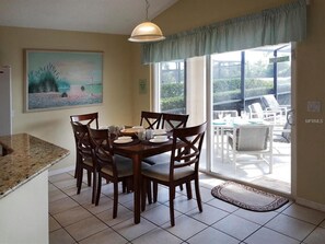 A dining area with a table set for four, a painting on the wall, and a view of the outdoors through a sliding glass door.