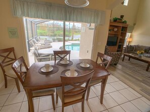 A dining area with a table set for four, a pool visible through the glass door, and a living room with a sofa and a coffee table.