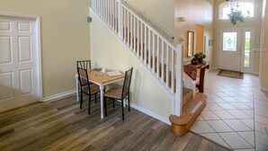 A spacious living area with a wooden dining table and chairs, a staircase with white railings, and a large window providing natural light. - Disney 6-bed Pool-spa Villa in Kissimmee, US (Kissimmee)