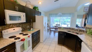 A kitchen with dark cabinets, a white stove, and a refrigerator. There is a dining area with a table and chairs visible through a window. - Disney 6-bed Pool-spa Villa in Kissimmee, US (Kissimmee)