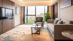 Una sala de estar moderna con un televisor de pantalla plana grande, un sofá, una mesa de centro y un ventanal con vistas a la ciudad.