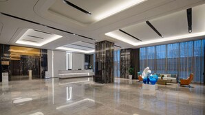 Un vestíbulo amplio con diseño moderno, que incluye una recepción, zona de estar y grandes ventanales.