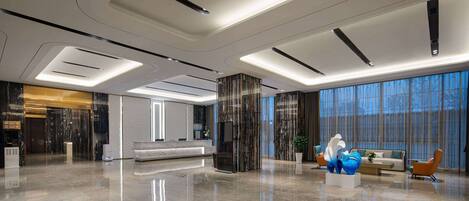 A spacious lobby with a modern design, featuring a reception desk, seating area, and large windows.