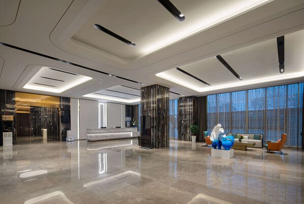 A spacious lobby with a modern design, featuring a reception desk, seating area, and large windows.