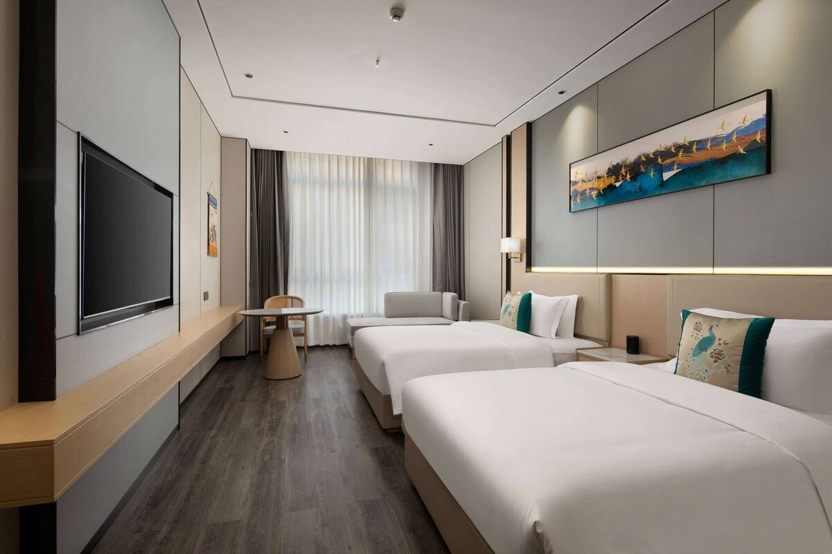 Ein Hotelzimmer mit zwei Betten, einem Flachbildfernseher, einem Schreibtisch und einem Bild an der Wand.