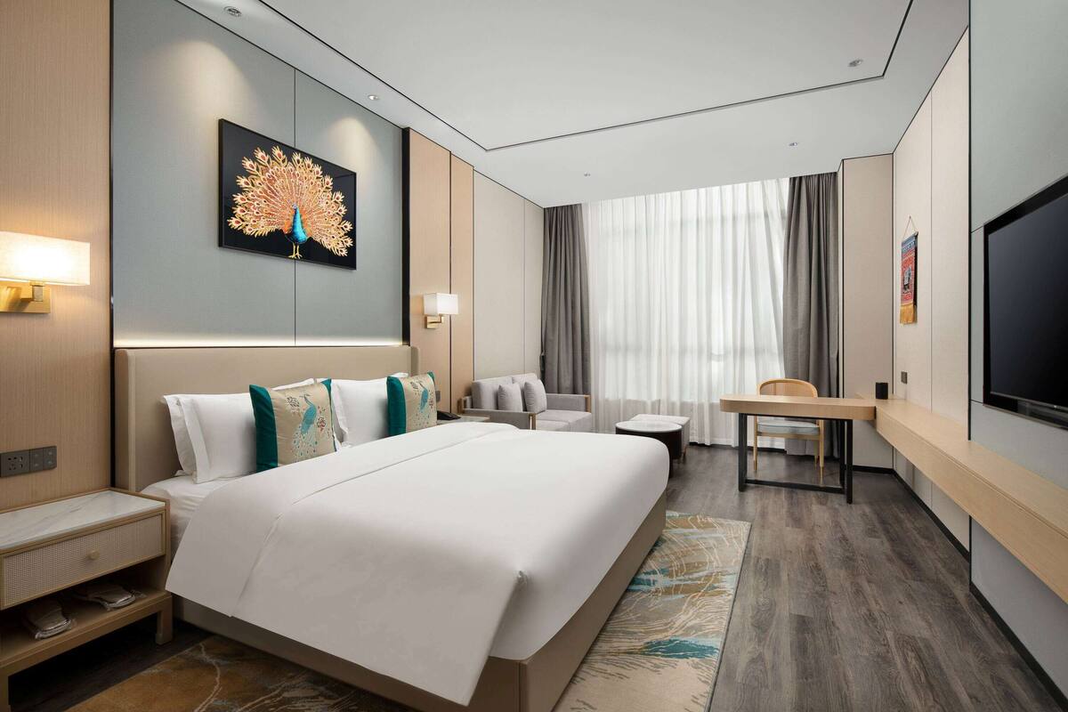 Ein modernes Hotelzimmer mit einem großen Bett, einem Schreibtisch, einem Sessel, einem Fernseher und einem Fenster mit Vorhängen.