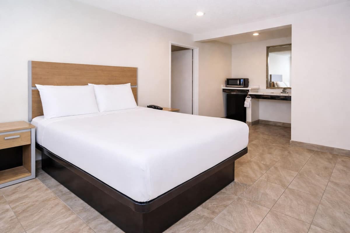 A hotel room with a large bed, a bedside table, a nightstand, a microwave, and a bathroom visible through an open door.