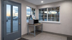 A hallway with a door, a window, and a small table with a microwave and other items.