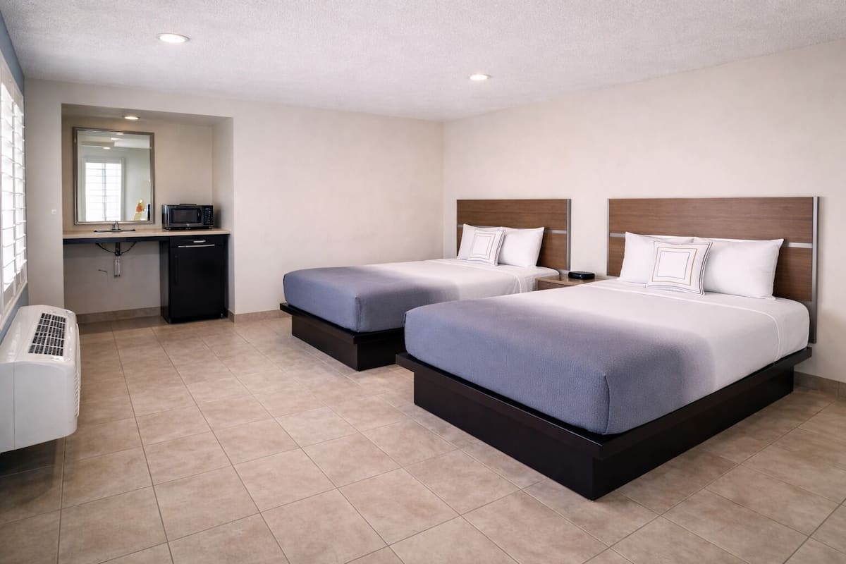 A hotel room with two beds, a kitchenette, and a large window.