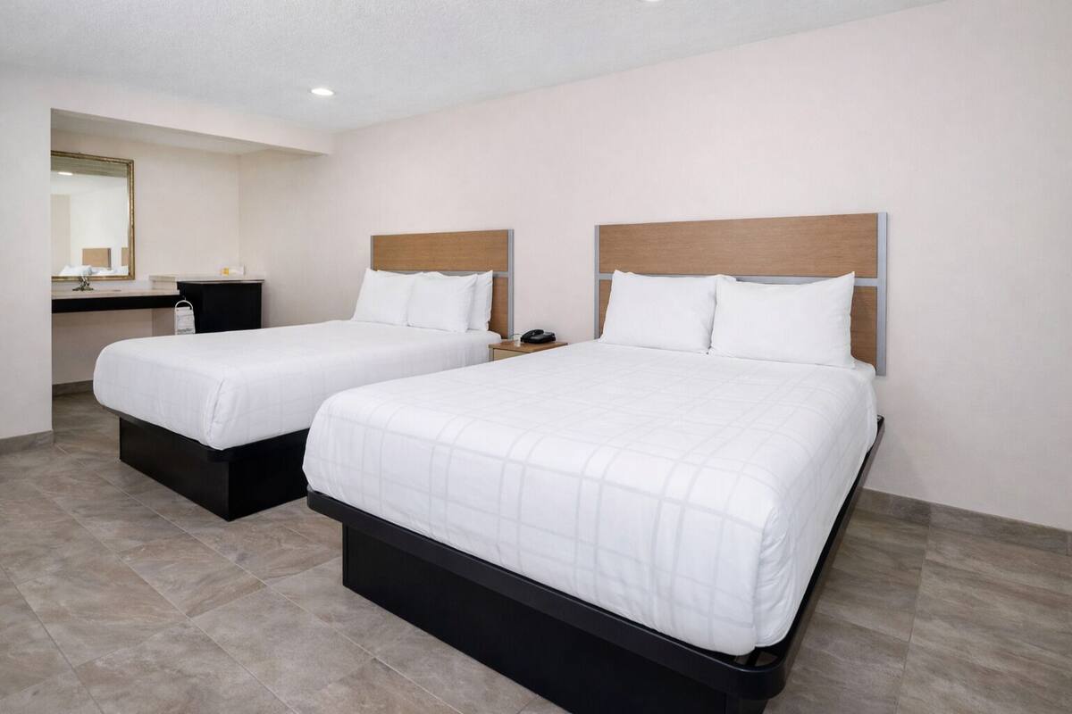 A hotel room with two beds, a desk, and a mirror.