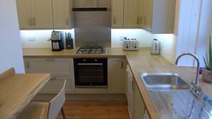 A compact kitchen with beige cabinets, a gas stove, a coffee maker, and a sink. - Snug - Tearlag Apartment (Helensburgh)