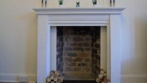 A fireplace with a white mantel, a round mirror above it, and logs stacked on either side. - Snug - Tearlag Apartment (Helensburgh)