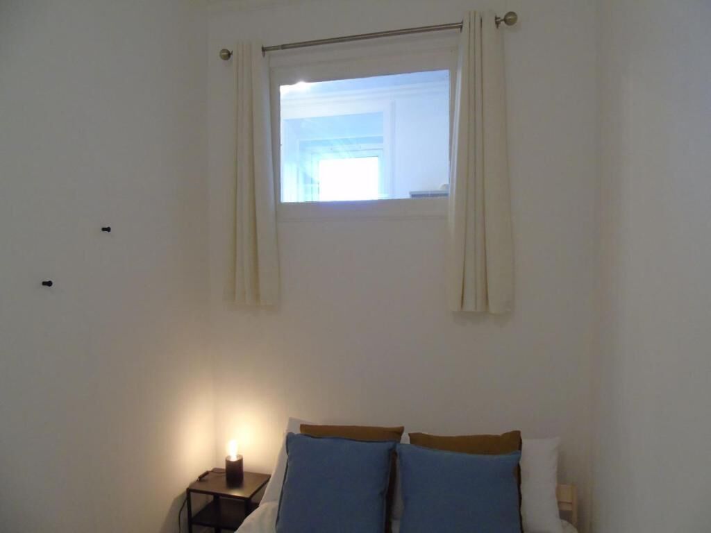 Un dormitorio con una cama individual, una mesita de noche con lámpara y una ventana con cortinas.