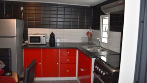 Een keuken met rode kastjes, een magnetron, een fornuis en een spoelbak.