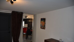Een kamer met een gesloten deur, een houten dressoir, een schilderij aan de muur en een blik op een eetgedeelte met rode stoelen en een tafel.