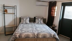 Een slaapkamer met een bed, een kledingkast, een airconditioning en een raam met gordijnen.