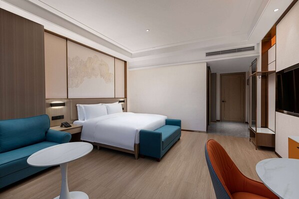 A modern hotel room with a bed, a sofa, a small table, and a TV.