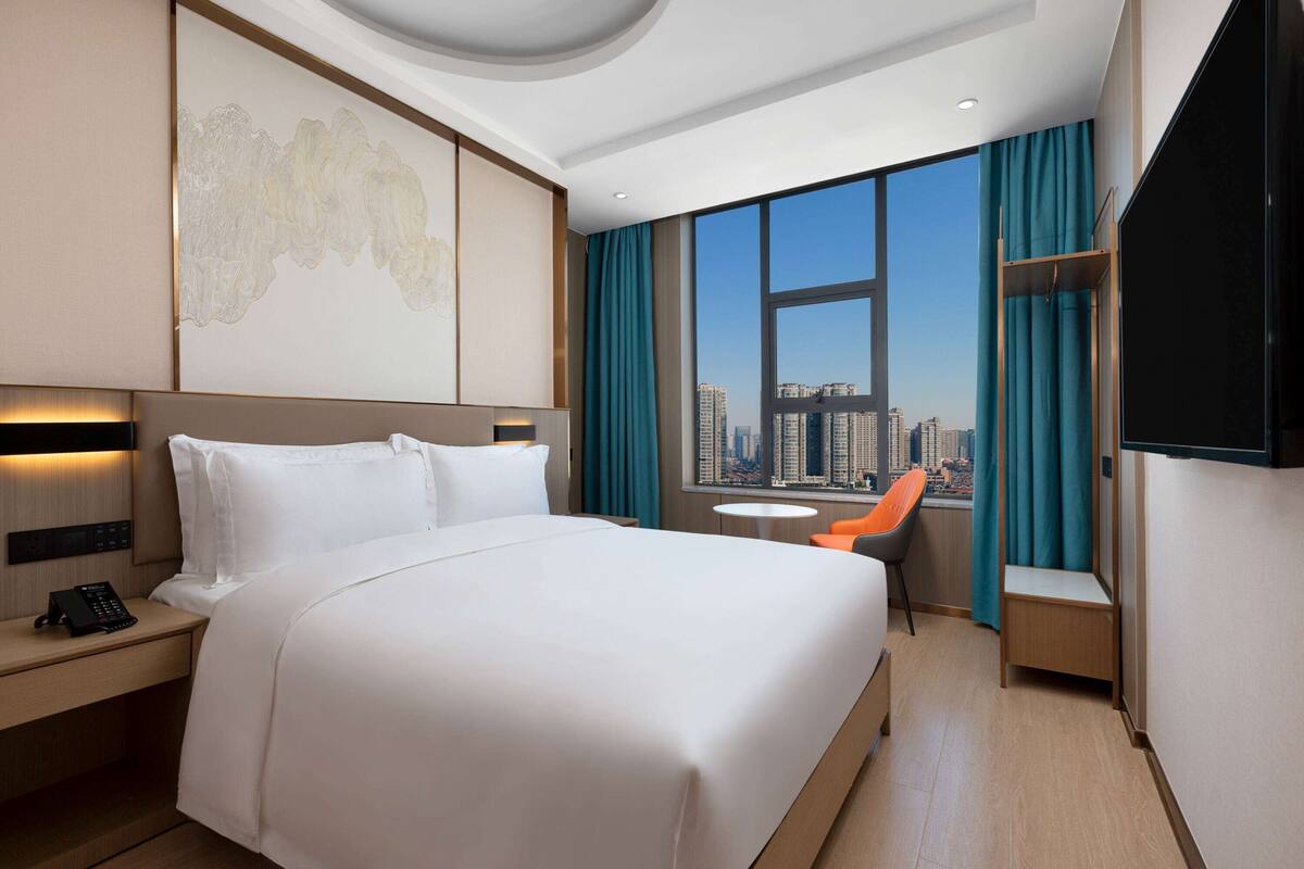 Une chambre d’hôtel moderne avec un grand lit, un bureau avec un téléphone, une chaise et un téléviseur.