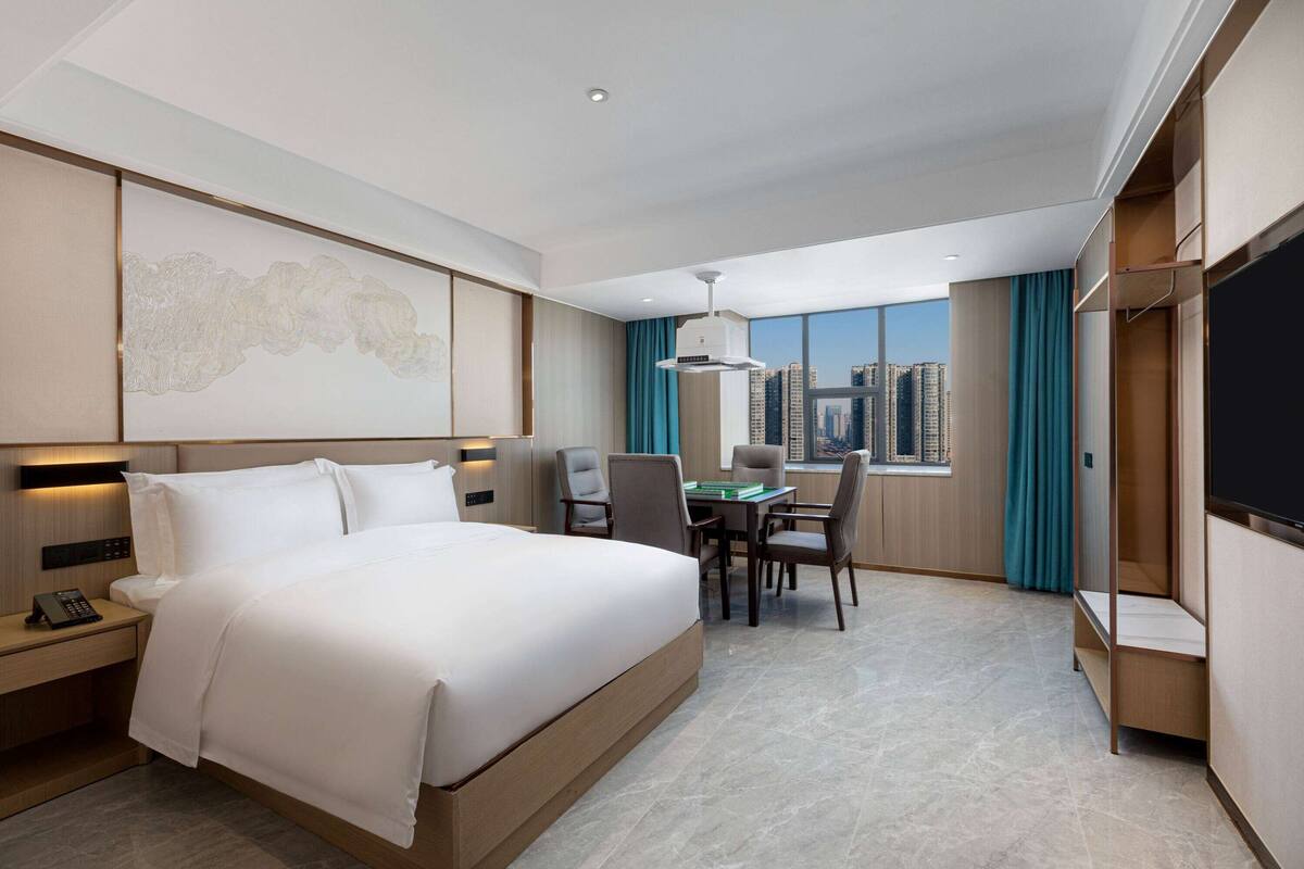 Une chambre d’hôtel moderne dotée d’un grand lit, d’un bureau avec des chaises, d’une télévision à écran plat et offrant une vue sur la ville.