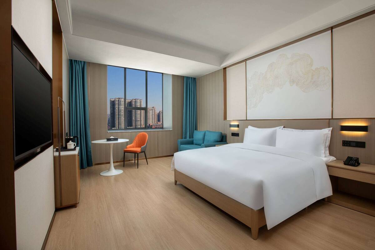 Une chambre d’hôtel avec un grand lit, un bureau avec une chaise, une petite table et un téléviseur.