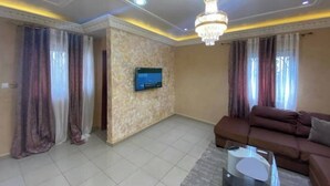 Un salon avec un canapé, un téléviseur fixé au mur et un lustre.