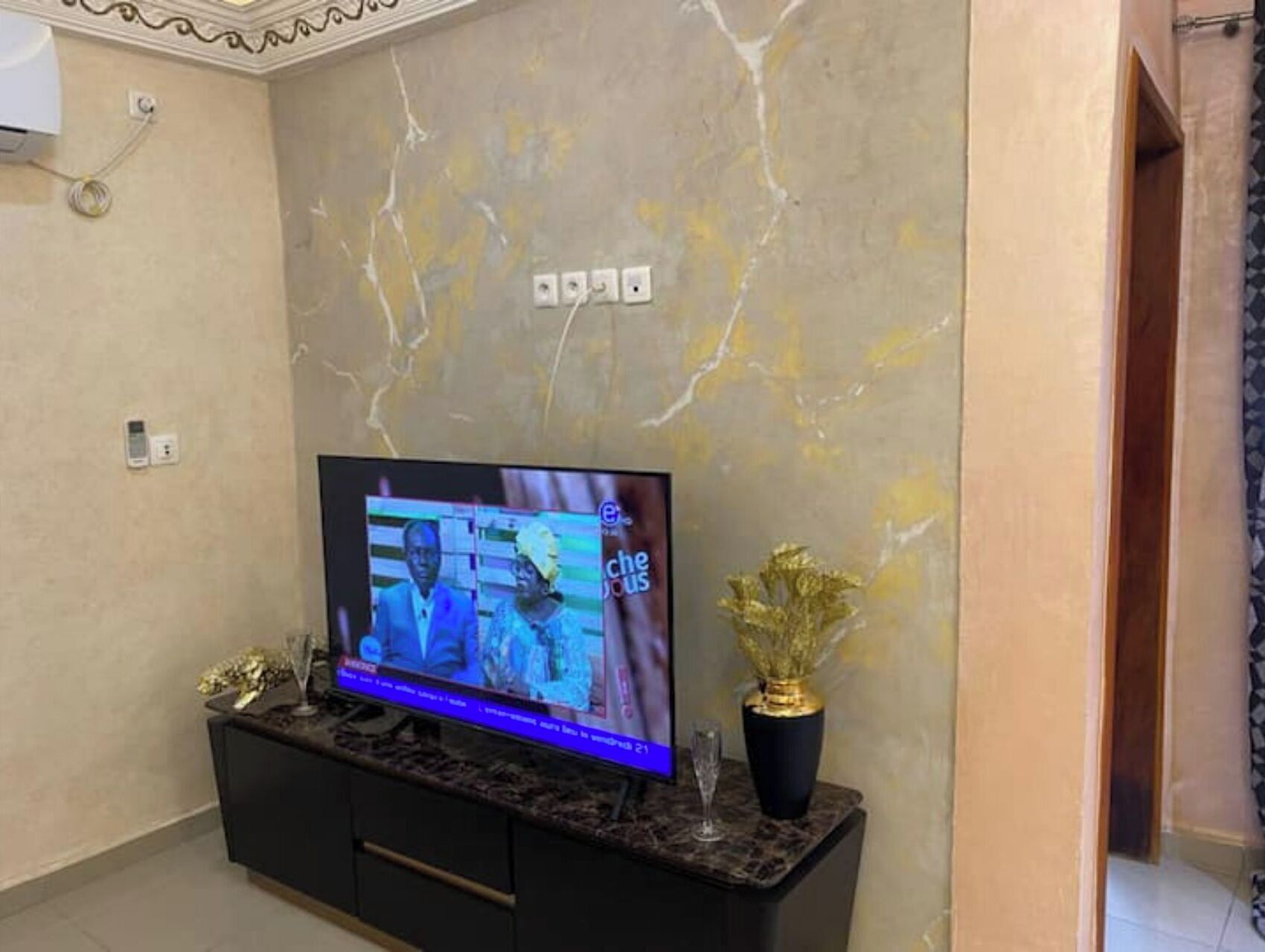 Een televisie op een zwarte tv-kast, met een marmeren muur op de achtergrond.