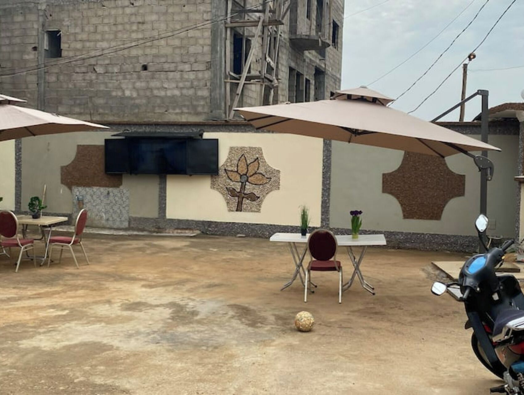 Un'area patio all'aperto con tavoli e sedie, una TV a muro e uno scooter parcheggiato nelle vicinanze.