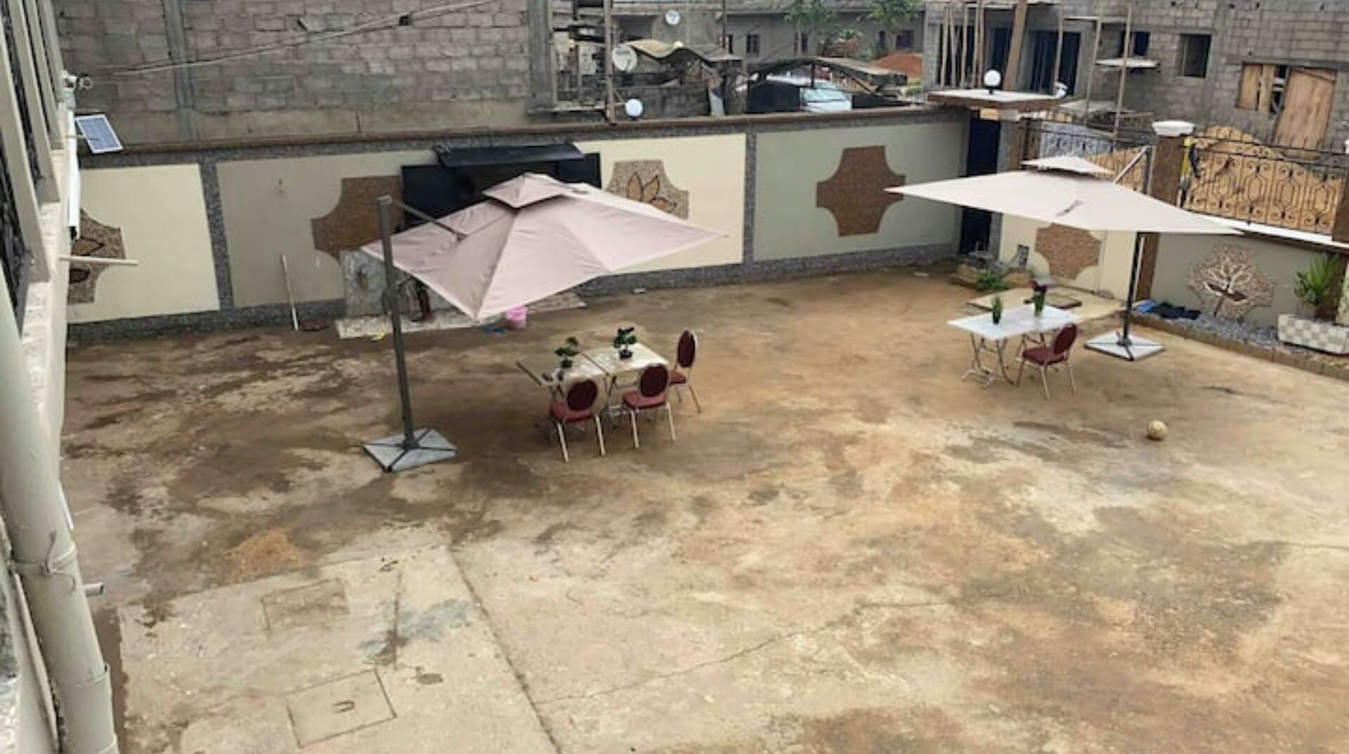 Ein Außenbereich mit einer Terrasse, zwei Tischen und Stühlen, jeweils mit Sonnenschirm.