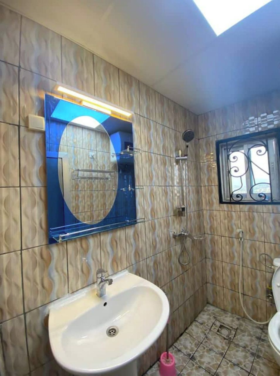 Casa de banho com lavatório, espelho, chuveiro e azulejos estampados.