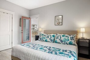 A bedroom with a bed, a nightstand, a wall-mounted lamp, and a door leading to a balcony. - Home Is Steps To Beach With Hot Tub (Gulf Shores)